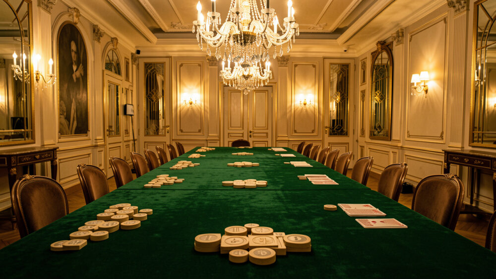 Salon parisien élégant aux tables recouvertes de velours vert, éclairé par des lustres dorés et préparé pour un événement de stratégie.